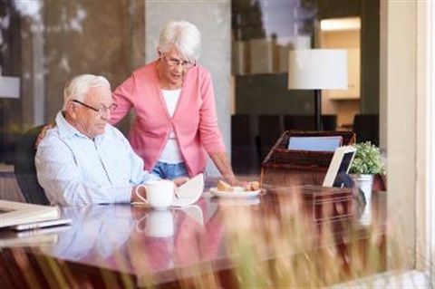 Older man writing on paper with wife looking on